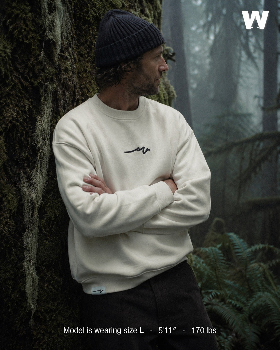 Model wearing the Natural Puff Dub Heavy Terry Crew against a mossy old-growth trunk — size L