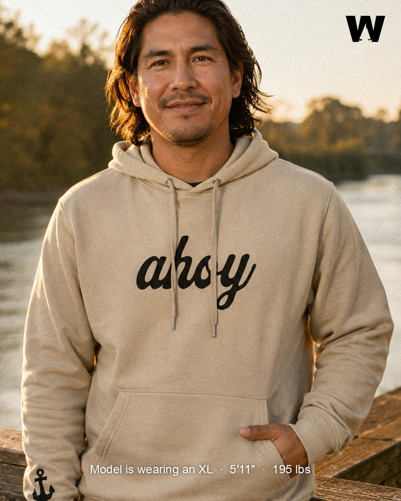 Silky Ahoy Hoodie in Desert Dust, worn by a model on the Snohomish riverfront at golden hour — black ahoy chest script and anchor sleeve embroidery